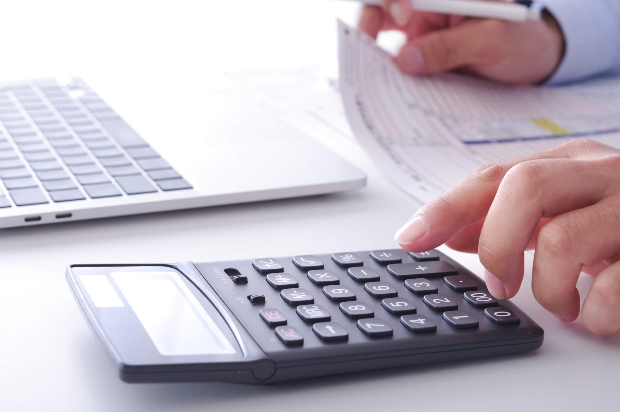 Hand typing on calculator to help fill out tax forms